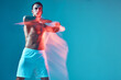 © Georgii - Athletic guy with naked torso raised arms performing dance on blue studio background. Copy space. Long exposure