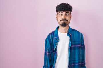 Poster - Young hispanic man with beard standing over pink background puffing cheeks with funny face. mouth inflated with air, crazy expression.