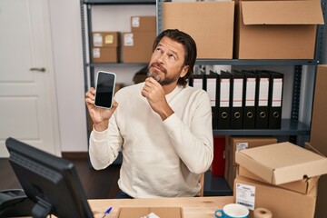 Poster - Handsome middle age man working at small business ecommerce holding smartphone serious face thinking about question with hand on chin, thoughtful about confusing idea