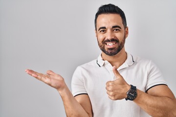 Sticker - Young hispanic man with beard wearing casual clothes over white background showing palm hand and doing ok gesture with thumbs up, smiling happy and cheerful