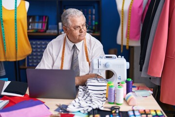 Canvas Print - Middle age grey-haired man tailor using sewing machine and laptop at tailor shop