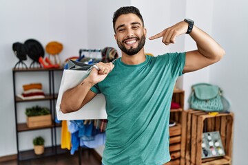 Sticker - Young handsome man with beard holding shopping bags at retail shop smiling cheerful showing and pointing with fingers teeth and mouth. dental health concept.