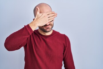 Wall Mural - Young bald man with beard standing over white background wearing glasses covering eyes with hand, looking serious and sad. sightless, hiding and rejection concept