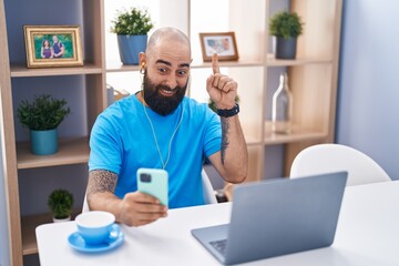 Canvas Print - Young hispanic man with beard and tattoos doing video call with smartphone smiling with an idea or question pointing finger with happy face, number one