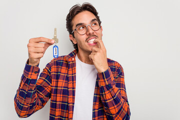 Wall Mural - Young hispanic man holding home keys isolated on white background relaxed thinking about something looking at a copy space.