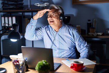 Canvas Print - Hispanic senior man wearing call center agent headset at night very happy and smiling looking far away with hand over head. searching concept.