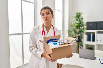 Canvas Print - Young doctor woman holding box with medical items looking at the camera blowing a kiss being lovely and sexy. love expression.