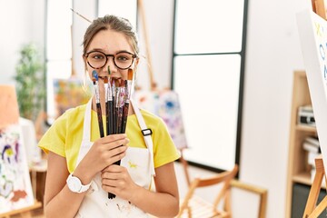 Poster - Adorable girl covering mouth with paintbrushes at art studio