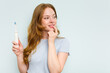 © Asier - Young caucasian woman holding electric toothbrush isolated on blue background relaxed thinking about something looking at a copy space.
