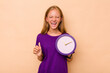 Little caucasian girl holding a clock isolated on beige background screaming very angry and aggressive.
