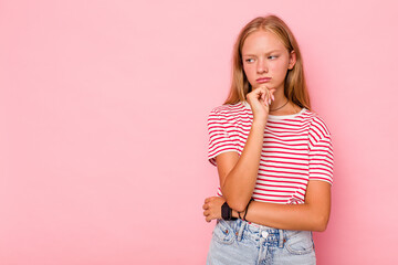 Caucasian teen girl isolated on pink background looking sideways with doubtful and skeptical expression.