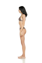 Poster - Side view of a young brunette woman in bikini swimsuit posing on a white background.