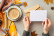 First person top view photo of girl's hands in sweater holding envelope paper card cup of coffee saucer plaid maple leaves pine cone anise cinnamon sticks on isolated grey background with blank space