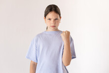 Portrait Of Angry Preteen Girl Threatening With Fist. Displeased Caucasian Child Wearing Blue T-shirt Posing Against White Background. Threats Concept
