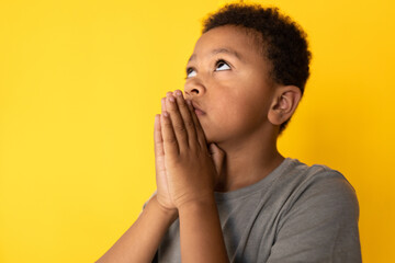 Close-up of concentrated preteen boy looking up and praying. Portrait of mixed race child wearing gray T-shirt looking upwards in hope. Faith and hope concept