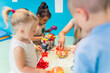 Relaxing sensory play with moldable kinetic sand at nursery school. Toddlers with their teacher having fun around the table using different tools for sculpting sand such as colorful and textured