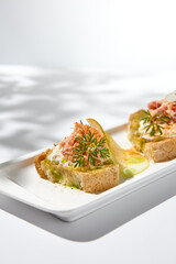 Canvas Print - Aesthetic composition with crab bruschetta on white background with shadows from flowers. Italian bruschetta with crab, avocado and cheese on fine dining in summer. Elegant menu concept.