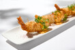 Traditional greek appetizer - kataifi wrapped shrimps on white plate. Crispy shrimp in kataifi crust in summer day. Shrimp appetizer fried in kataifi dough. Crispy prawns in modern style.