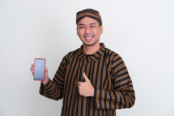 A man wearing Javanese traditional costume smiling while showing empty phone screen