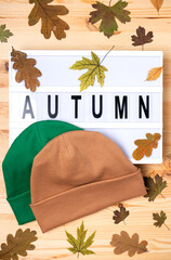 Wall Mural - Beanie hats with the inscription Autumn with yellow leaves on a wooden table. Shop advertisement template. Vertical photo