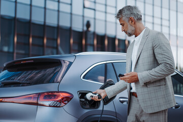 Man holding power supply cable at electric vehicle charging station, closeup