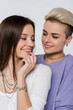 © LIGHTFIELD STUDIOS - happy lesbian woman looking at happy girlfriend touching lip isolated on grey.