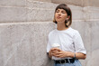 © PhotoBook - Romantic dreamy girl with short hair wearing white t-shirt posing over beige wall outdoor with coffee