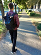 A teenage boy with a backpack goes to school on the street. Rear view in perspective