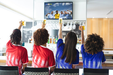 Group of diverse friends sitting in the bar, drinking beer and watching football match