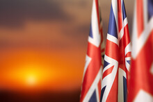 National Flags Of United Kingdom On A Flagpole On Sunset Sky Background. Lowered UK Flags. Background With Place For Your Text.