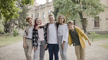 Wall Mural - Happy multiethnic school children hugging and smiling on camera, friendship