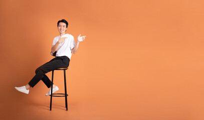 Wall Mural - image of asian man sitting on a stool, isolated on orange background