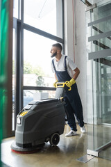 Wall Mural - full length of bearded man with professional floor scrubber machine in office.