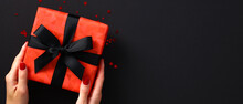 Luxury Red Gift Box Wrapped Black Ribbon Bow In Female Hands Over Black Background With Confetti. Black Friday Sale Banner Design