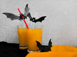 © Виктория Чемаева - Halloween party cocktail. Orange drink in transparent glass decorated with bats, Halloween party drinks idea. Paper bats on cocktail tubes