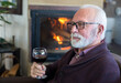 © Solid photos - Senior man drinking wine while sitting by the fireplace