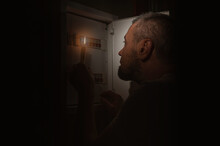 Blackout, No Electricity. A Man With A Candle In The Dark Examines The Electrical Switchboard At Home.