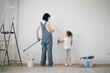 © sofiko14 - Full length portrait back view of young mother and her small cute daughter enjoying time together while painting wall.