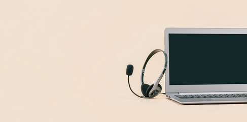 Wall Mural - Front view of slim laptop with headset on beige. Monochrome background. Distant learning. working from home, online courses or support. Audio podcast headphones . Helpdesk or call center banner