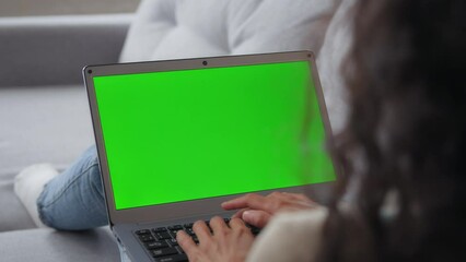 Over shoulder shot back view from behind unrecognizable brunette girl woman lying sitting on couch working on pc business chatting looking at green screen chroma key copy space using laptop computer