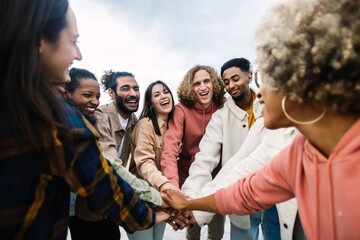 Happy young group of multiracial people stacking hands outdoors - Community and unity concept