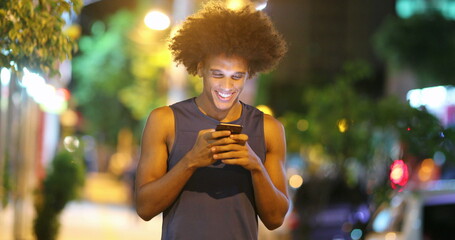 Young african man looking at cellphone device at night in city sidewalk