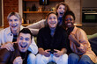 © Seventyfour - Group of young intercultural excited friends sitting in front of tv set and playing video game together while black woman using joystick