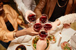 © Seventyfour - Above view of hands of young friends clinking with wineglasses over dinner table served with homemade food during celebration