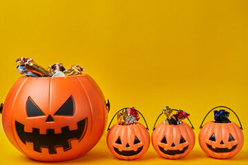 Parents and kids Halloween concept. Big Pumpkin head basket with three small baskets full of candy over yellow background and copyspace