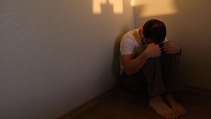 alone depressed man sitting in corner dark room because of problem and sadness in life. Sadnes and spite concept