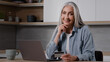 © Yuliia - Elderly lady buyer grandmother shopper mature woman sit in kitchen pay utility bills on laptop use banking app for online charity enter security card number at computer internet financial transaction