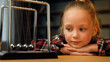 © Yuliia - Concentrated child girl female little patient blonde cute beautiful small lady preschooler sitting on psychotherapy session indoors looking at swinging metal steel balls law kinetic energy hypnotized