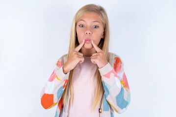 Wall Mural - little kid girl wearing colorful yarn jacket over white background crosses eyes and makes fish lips funny grimace