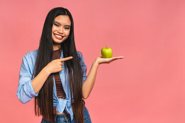 Portrait of a happy young asian chinese korean japanese woman holding or eating green apple isolated over pink background.